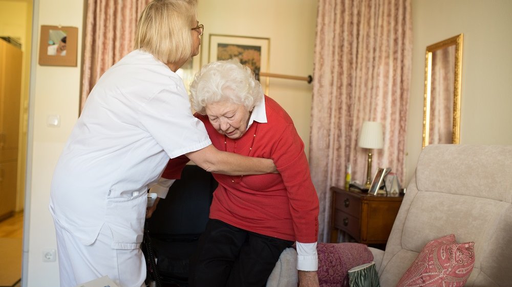 Pflegerin hilft Seniorin in den Sessel