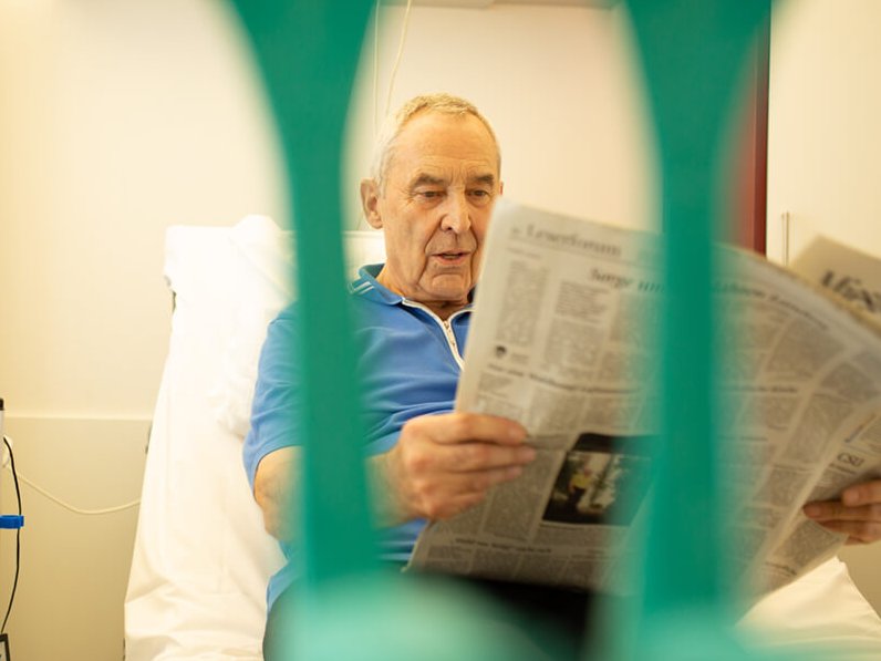 Ein Patient beim Zeitunglesen im Bett